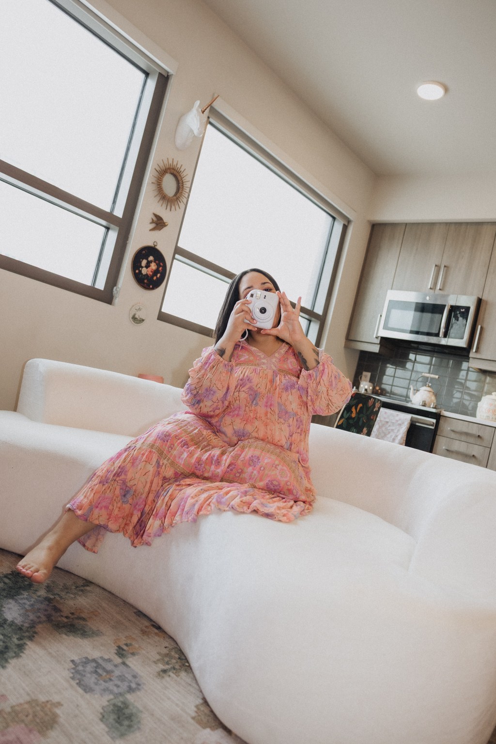 The Girl in Gucci Glasses wearing a flowing Spell dress holding an Instax instant camera, captured in a candid, natural moment that blends fashion and analog photography, evoking a soft nostalgic aesthetic.